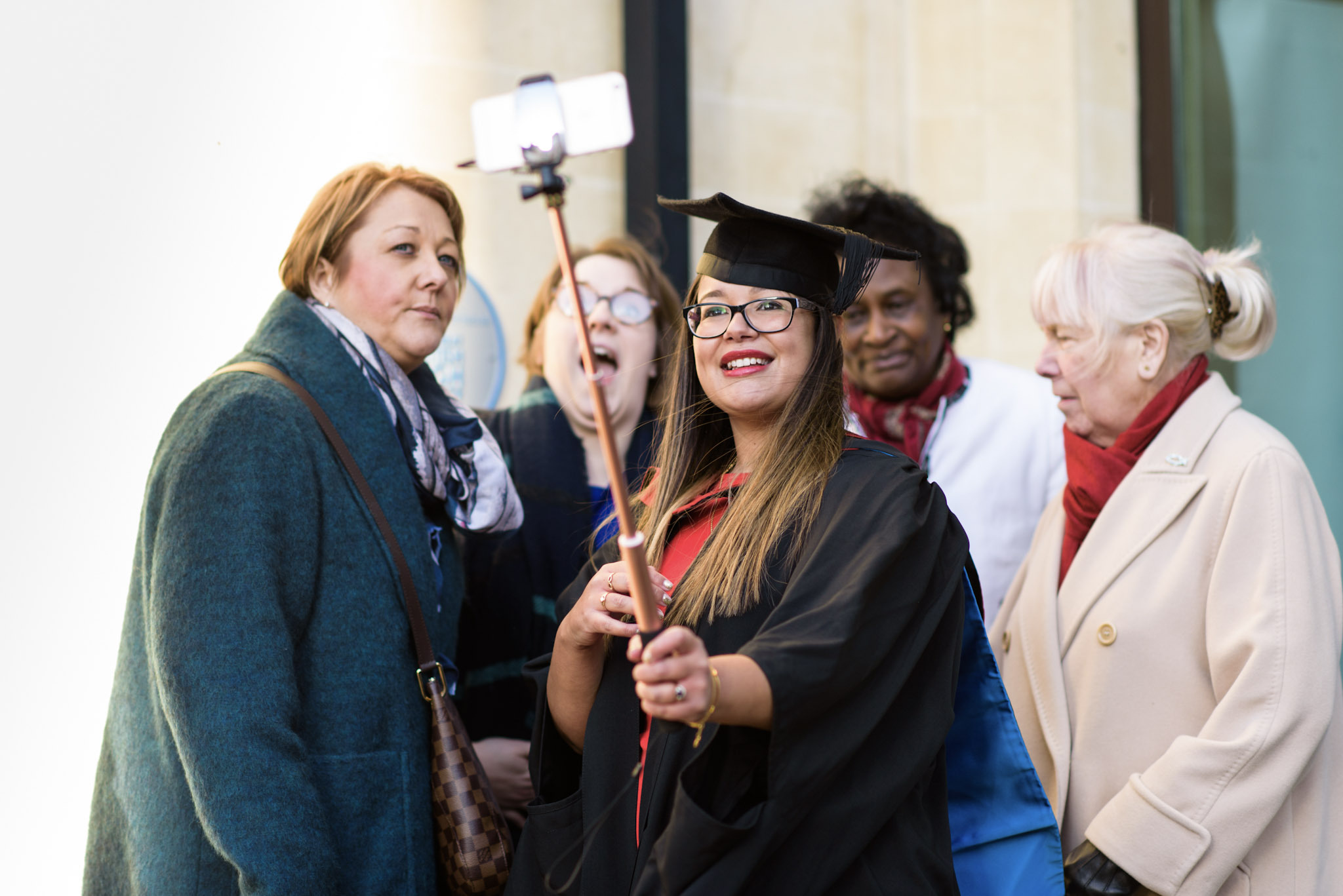 Graduating Student using a selfie stick with a group of women.